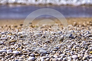 Background of white sea pebbles on the beach. Selective focus, blurred sea waves on background. Sea gravel texture background.