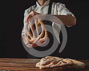 On background of wooden brown table, men`s hands hold bread fougas