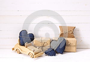Background with wooden toy car, gift boxes and denim hearts.