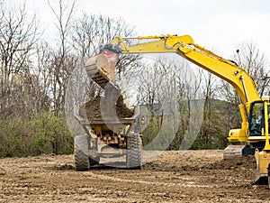 Backhoe Bucket Dumping Soil into Truck Bed