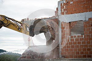 Backhoe demolishing a brick house