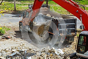 Backhoe excavator scoop loading from building in the construction debris dump truck
