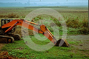 A backhoe loader excavator digger, a heavy industrial vehicle on a green agricultural field