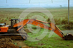 A backhoe loader excavator digger, a heavy industrial vehicle on a green agricultural field