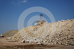 A backhoe loader, a loader backhoe, digger on a heap of sand and stones on a natural background.