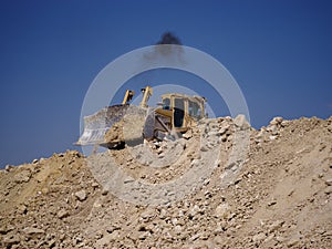 A backhoe loader, a loader backhoe, digger on a heap of sand and stones on a natural background.