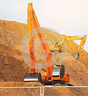 Backhoe standing on pile of woodchips during pile making work