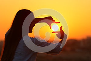 Woman framing sun with fingers at sunset photo