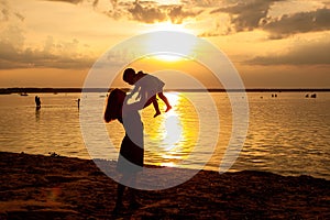 Backlight side view portrait of a happy mother raising her kid son at sunset