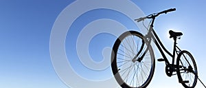 Backlight silhouette of a classic black bicycle ride. Blue sky in the background. Panoramic view. Space for text