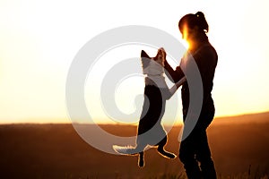 Backlight Silhouette of a woman with her jumping dog, playing on