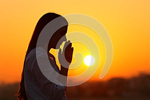 Backlight of a woman praying at sunset