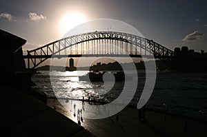 Backlighted silhouette of historic Sydney Harbor Bridge by promenade. Backlit heritage steel truss arch bridge spanning over water