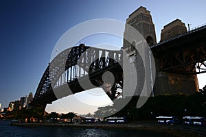Backlighted silhouette of historic Sydney Harbor Bridge in twilight. Backlit heritage steel truss arch bridge spanning over water