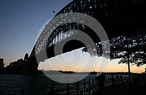 Backlighted silhouette of historic Sydney Harbor Bridge in twilight. Backlit heritage steel truss arch bridge spanning over water