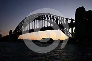 Backlighted silhouette of historic Sydney Harbor Bridge in twilight. Backlit heritage steel truss arch bridge spanning over water
