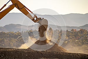 Backlit Backhoe scooping dirt and dust with hills in the background