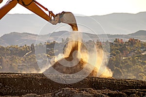 Backlit Backhoe scooping dirt and dust with hills in the background