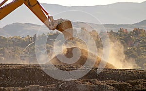 Backlit Backhoe scooping dirt and dust with hills in the background