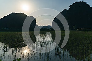 Backlit Mountains of Ninh Binh with water filled rice fields in the forground at sunset