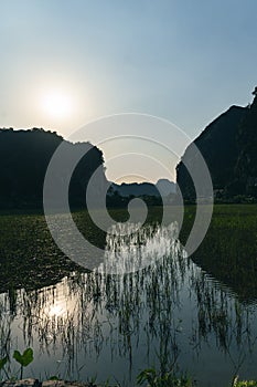 Backlit Mountains of Ninh Binh with water filled rice fields in the forground at sunset