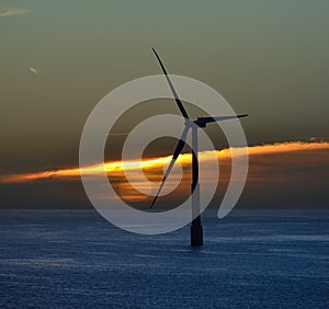 Backlit offshore turbine at sunrise