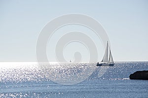 Backlit sailboat on bright and sunny sea with horizon