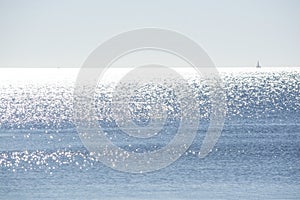 Backlit sailboat on bright and sunny sea with horizon