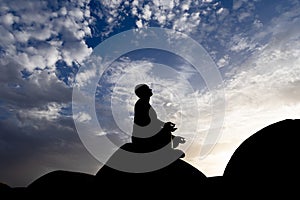 backlit shot of isolated man meditating at wall with sunset dramatic sky at dusk