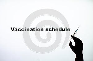 Backlit single shot image of Vaccination schedules with a hand holding an vaccine