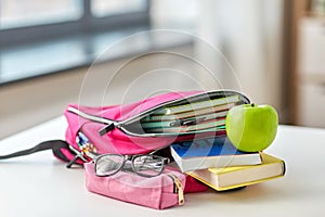 Backpack, apple and school supplies on table