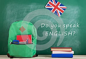 backpack, blackboard with text "Do you speak English?", flag of the Great Britain, calculator, books and notebooks