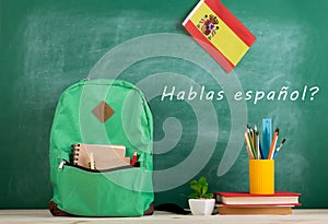 backpack, blackboard with text "hablas espaÃ±ol", flag of the Spain, books and school supplies