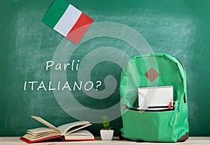 backpack, blackboard with text "Parli italiano?", flag of the Italy, books and notebooks