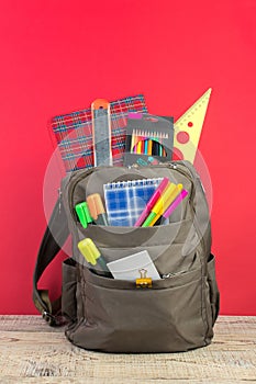 Backpack with different colorful stationery on table. Bright Red background. Back to school