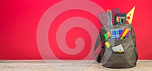 Backpack with different colorful stationery on table. Bright Red background. Back to school. Banner design