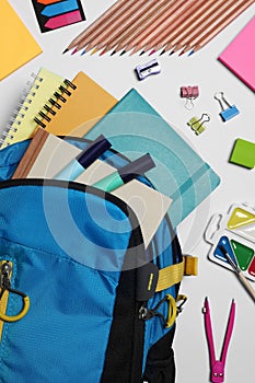 Backpack with different school stationery on white background, flat lay