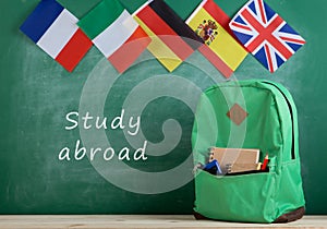 backpack, flags of Spain, France, Great Britain and other countries and school supplies on the background of the blackboard