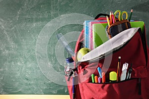 Backpack full of school supplies and blackboard front view detail