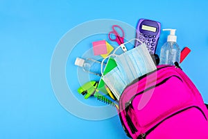 Backpack full of school supplies and COVID 19 prevention items. Top view, spilling onto a blue background. Back to school during p
