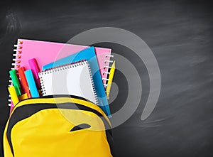 Backpack full of school supplies over black school board background