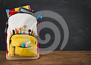 Backpack full of school supplies over black school board background