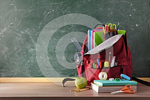 Backpack full of school supplies on table and blackboard front