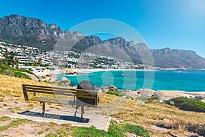 Backpack of lonely traveller on a bench with a view of Camps bay beautiful beach in Cape Town
