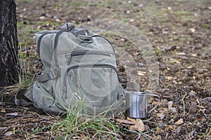 A backpack, a mug, a flashlight are lying on the grass in the forest. Tourist equipment. Walk in the forest and traveling.