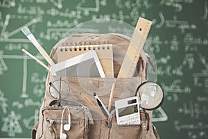 Backpack school with supplies in front of green chalkboard