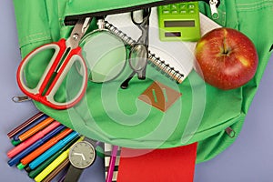 Backpack and school supplies: magnifying glass, notepad, felt-tip pens, eyeglasses, scissors, calculator, watch on blue paper back