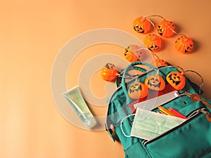 Backpack with school supplies , medical mask , sanitizer gel and halloween pumpkin lights on orange background.COVID-19 prevention