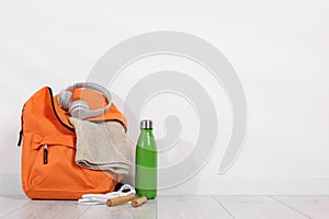 Backpack and sports equipment on floor near white wall, space for text