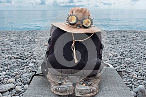 A backpack, a straw hat with glasses and an old sneaker lie by the seashore